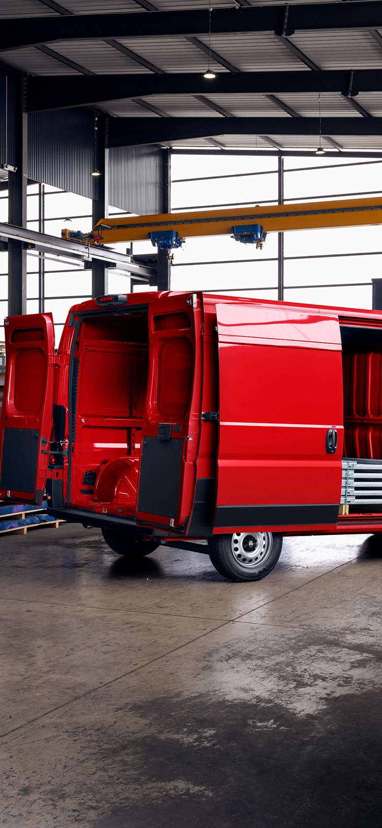 Vista trasera de tres cuartos de un Citroën Jumper rojo con las puertas de carga abiertas en un almacén, destacando el amplio espacio de carga, durabilidad y versatilidad profesional.