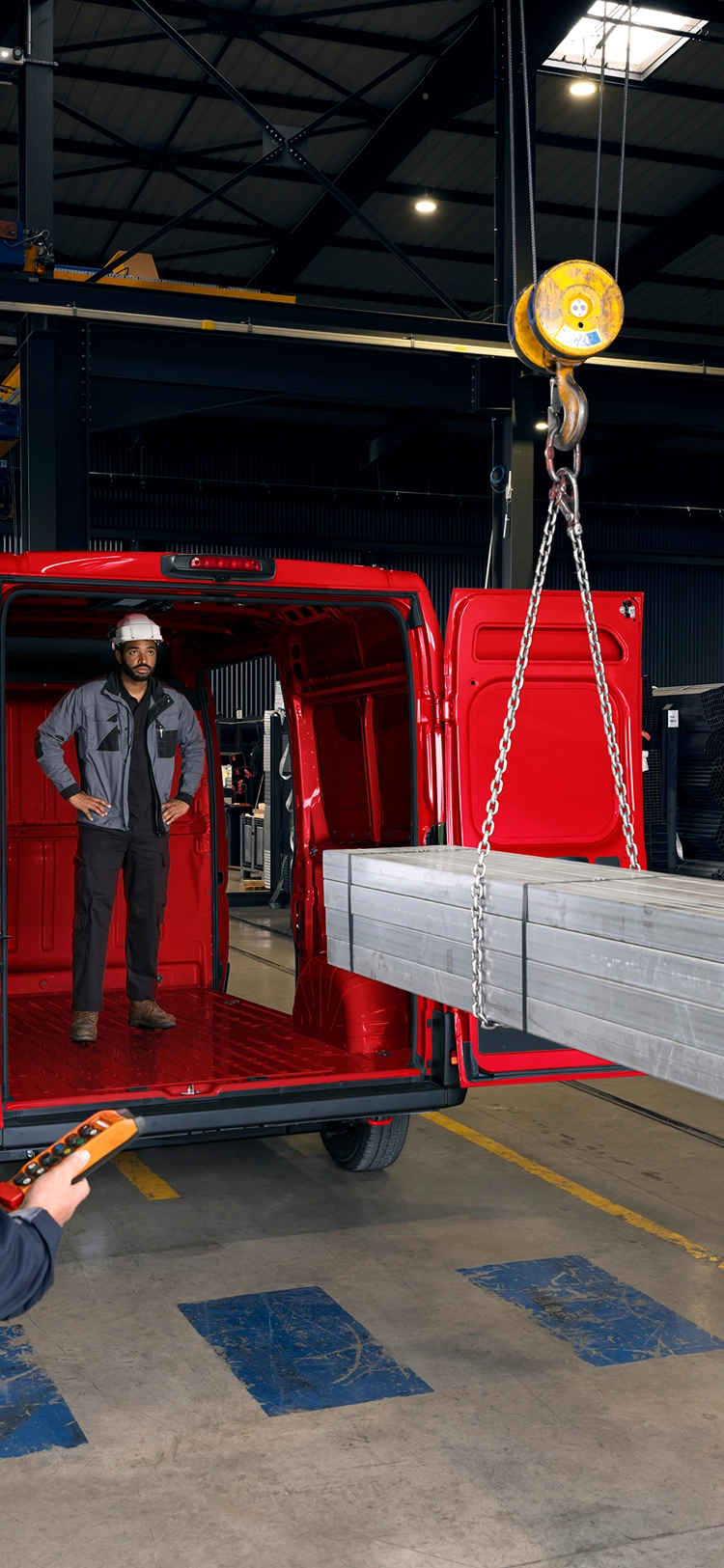 Vista trasera de un Citroën Jumper rojo siendo cargado con vigas metálicas en un entorno industrial, destacando el gran volumen de carga y capacidad para trabajo pesado.