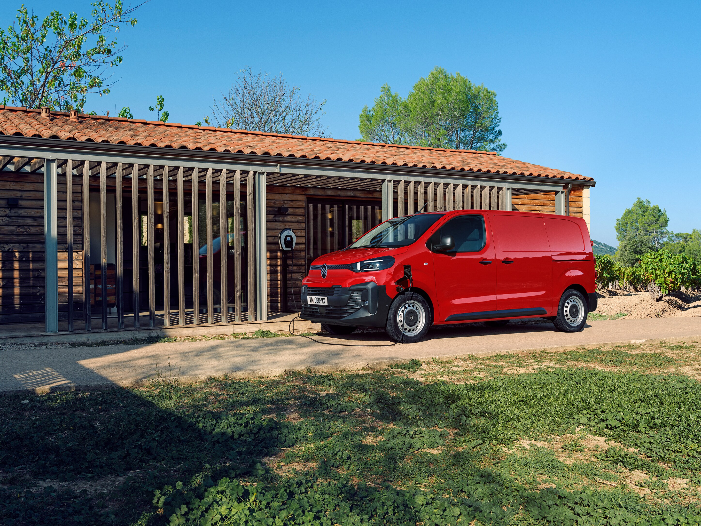Vista exterior tres cuartos lateral de un Citroën ë-Jumpy rojo cargando frente a un edificio, mostrando movilidad eléctrica, practicidad diaria y presencia profesional segura.