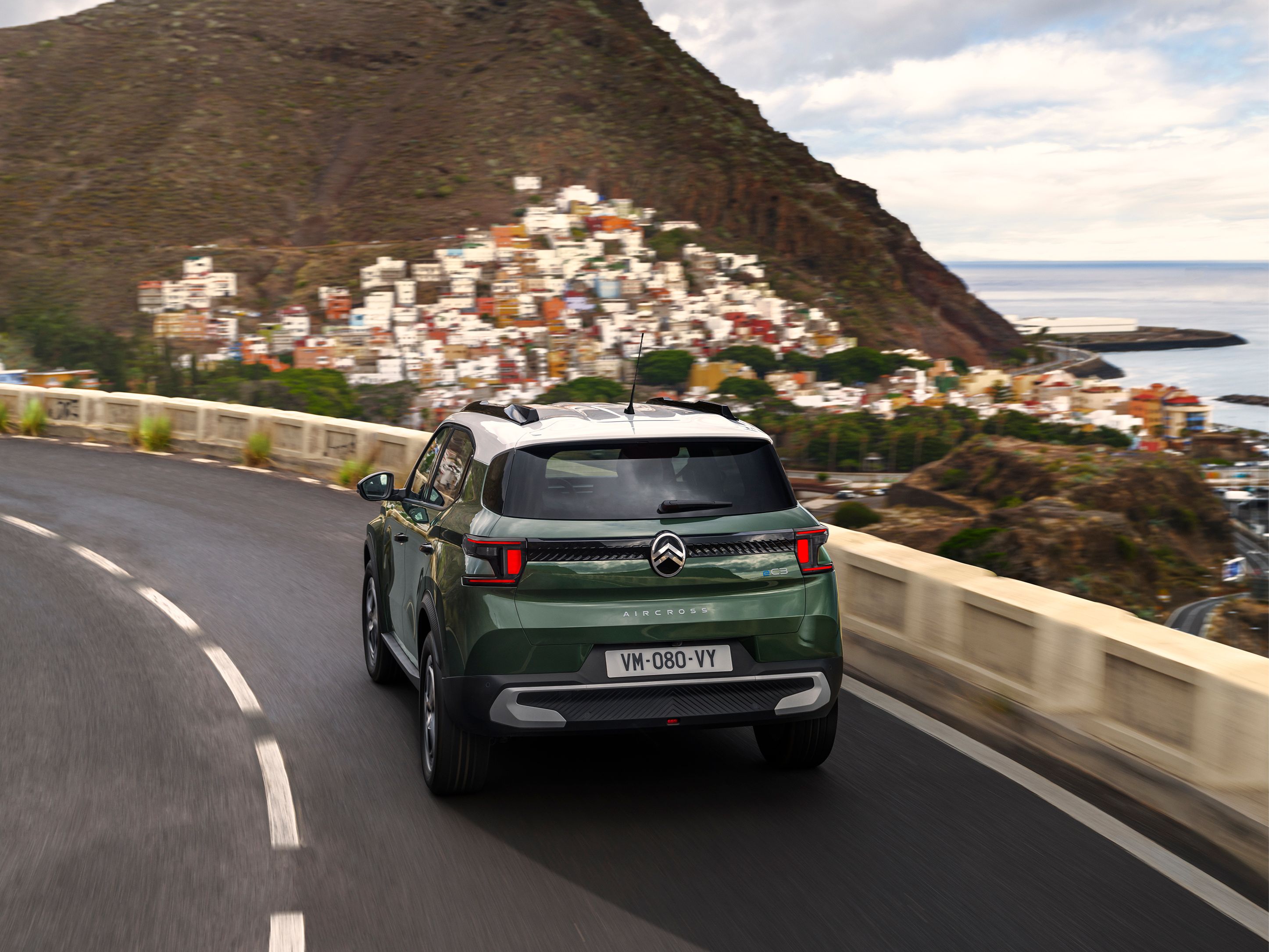 Vista trasera tres cuartos en conducción del Citroën C3 Aircross SUV en una carretera costera para una movilidad diaria con confianza, suave y asequible.