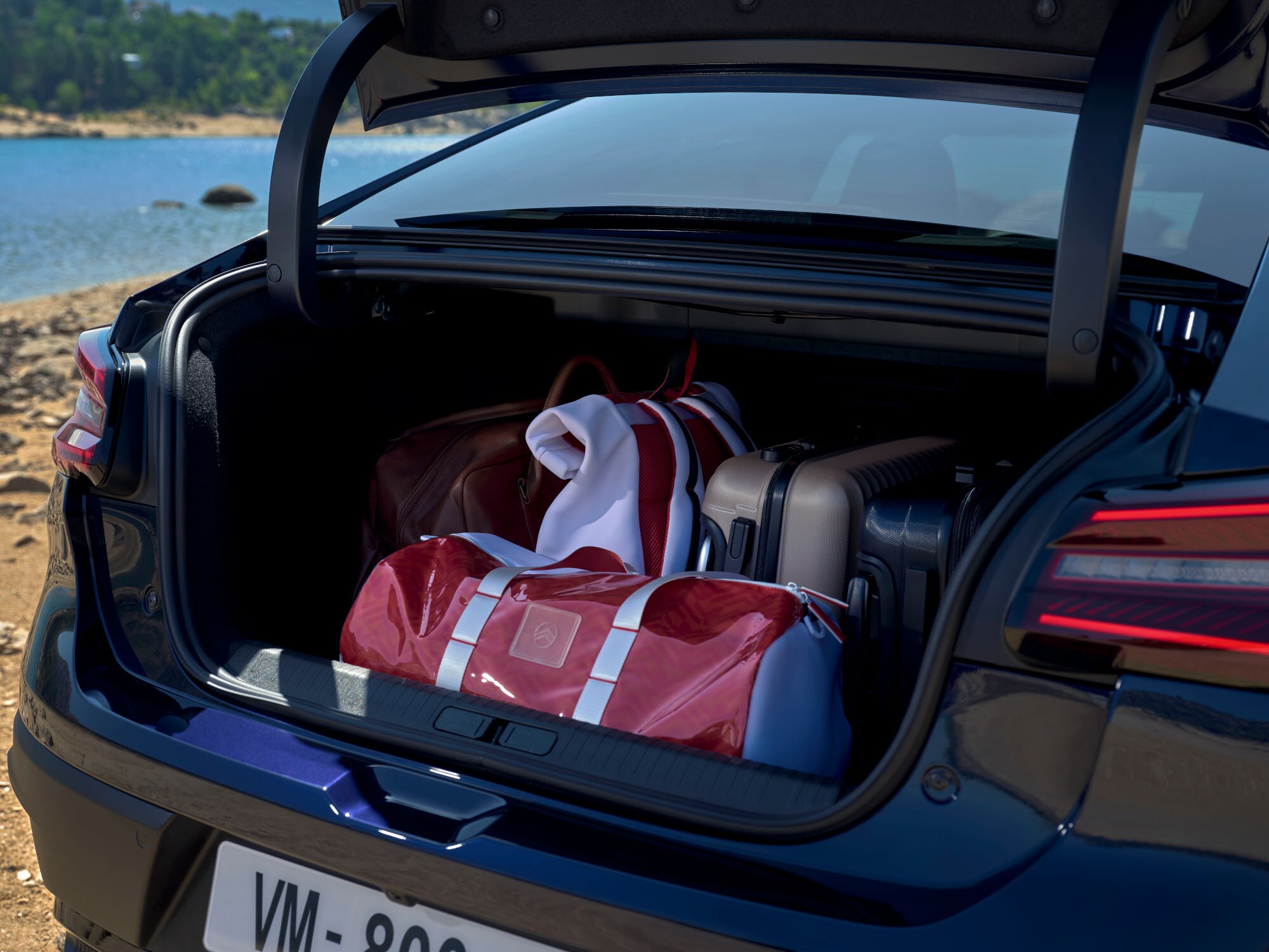 Maletero abierto del Citroën ë‑C4 X cargado con bolsas de viaje junto a una ubicación lacustre.