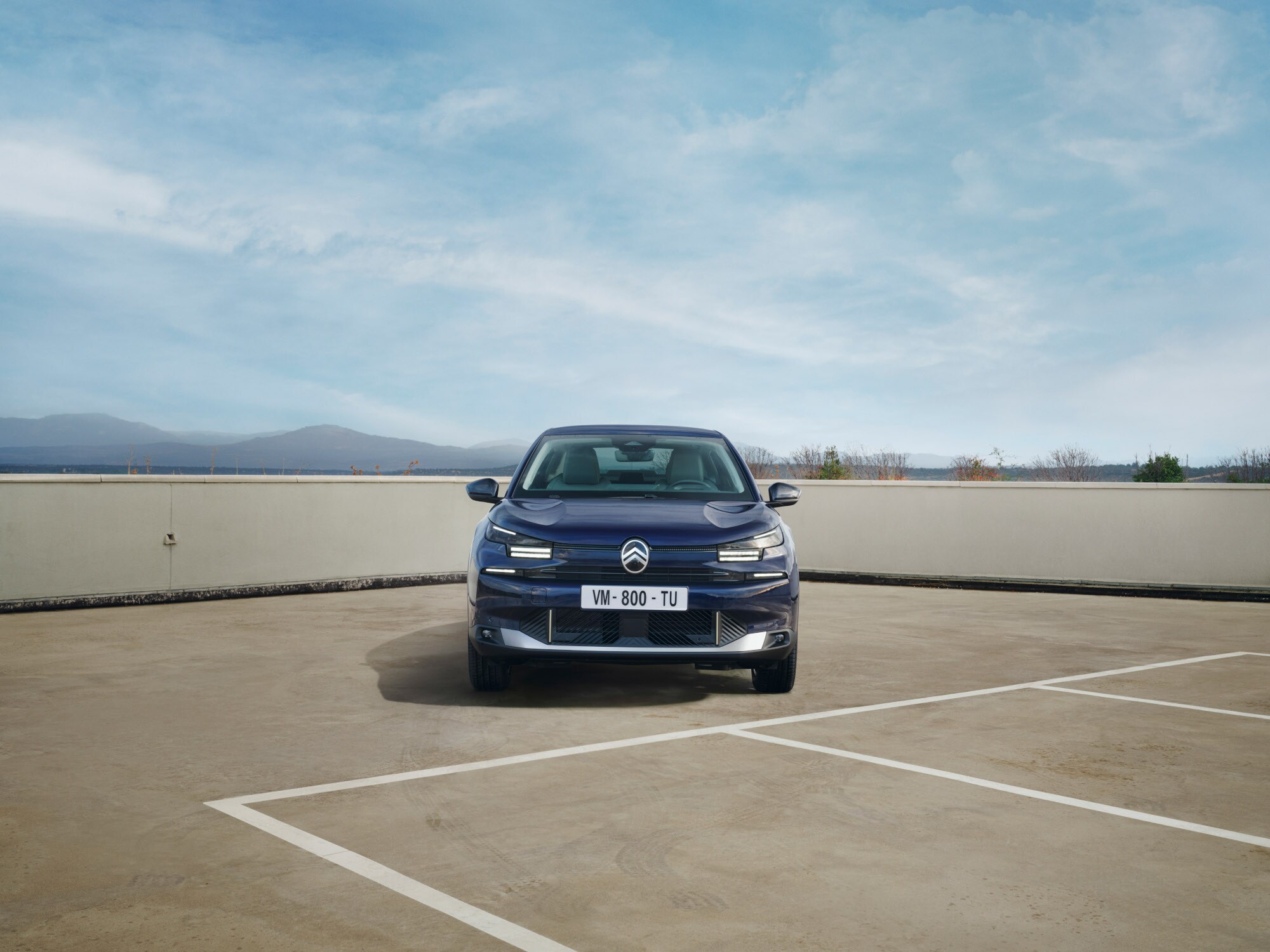 Vista frontal del Citroën ë-C4 X en parking de azotea destacando presencia fastback atrevida para una movilidad con confianza y asequible.