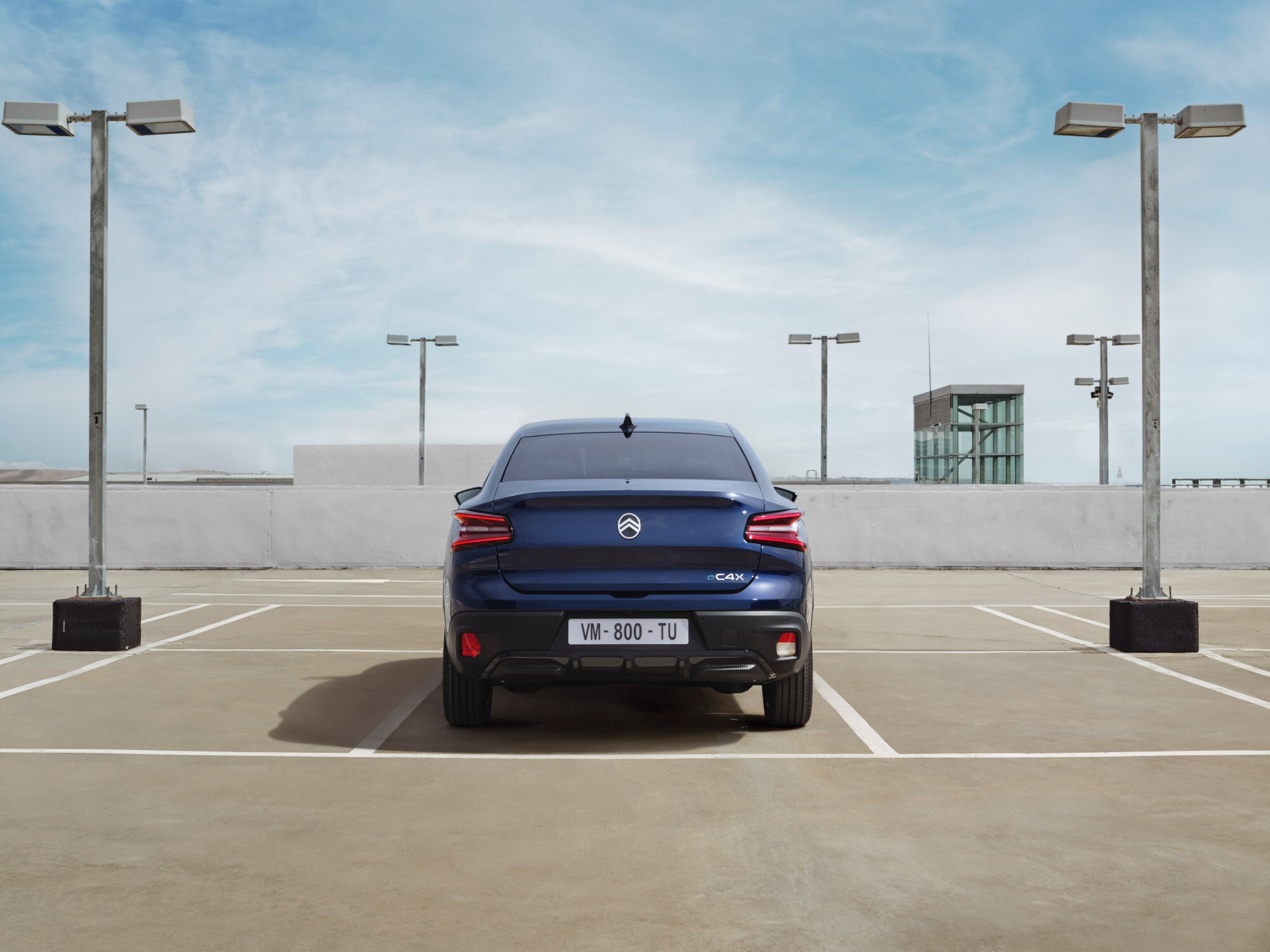 Vista trasera del Citroën ë-C4 X en parking de azotea mostrando diseño fastback distintivo para una movilidad elegante y asequible.