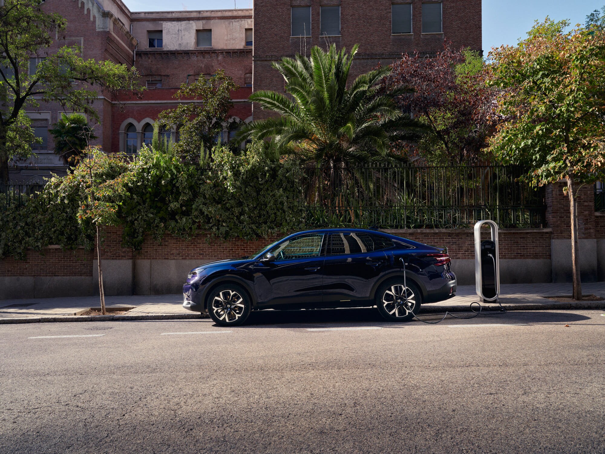 Vista lateral del Citroën ë‑C4 X fastback eléctrico cargando en la calle, destacando movilidad urbana conveniente y asequible.
