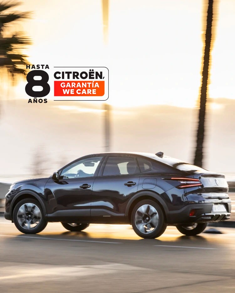Citroën ë‑C4 X conduciendo por una carretera costera al atardecer con la insignia de cobertura Citroën de 8 años mostrada.